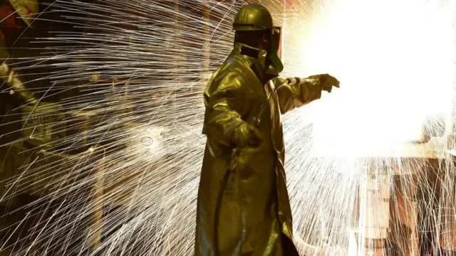 An employee works in front of the blast furnace past rolls of sheet steel at a mill of German steel producer Salzgitter AG on March 1, 2018 in Salzgitter,