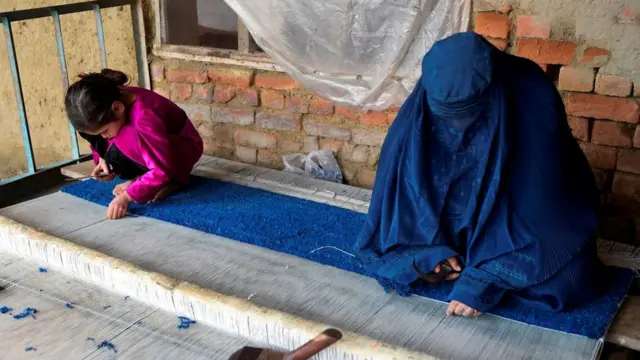 An Afghan refugee woman and her daughter make carpet at her home in a refugee camp in Peshawar