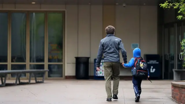 Un padre de espaldas acompaña a un niño a la escuela.