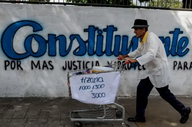 Un hombre pasa con su carro de supermercado frente a una pintada que hace referencia a las elecciones para una Asamblea Constituyente en Venezuela.