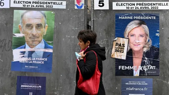 A pedestrian walks past campaign posters of French far-right party Reconquete! presidential candidate Eric Zemmour (L) and French far-right party Rassemblement National (RN) presidential candidate Marine Le Pen (R), three days ahead of the first round of the French presidential election, in Paris on April 7, 2022.