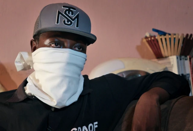 مردی سیاه‌پوست که صورتش را با دستمالی سفید پوشانده است و کلاه به سر دارد