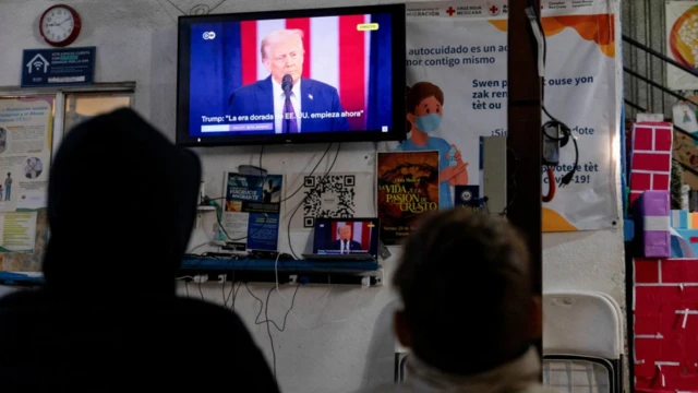 Dos migrantes que esperaban solicitar asilo en Estados Unidos siguen el discurso de Donald Trump tras su toma de posesión como presidente desde una televisión en el albergue Juventud 2000 de Tijuana, México, el 20 de enero de 2025. REUTERS/Zaydee Sanchez