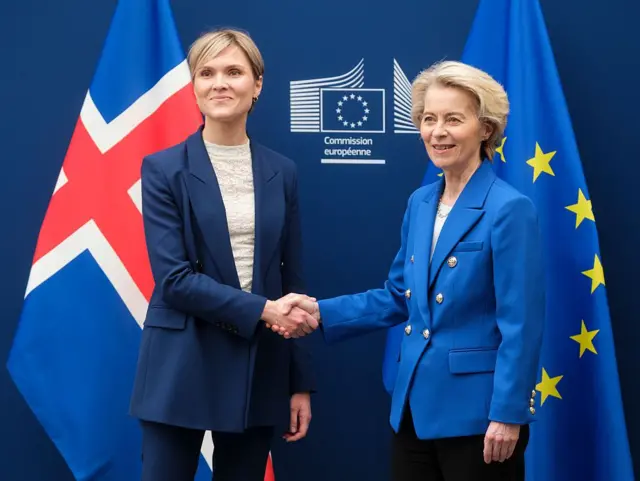 La primera ministra islandesa, Kristrún Frostadóttir, a la izquierda, junto a la presidenta de la Comisión Europea, Ursula von der Leyen. Sonríen a las cámaras con las manos estrechadas. Tras ellas, las banderas de Islandia y de la UE. 