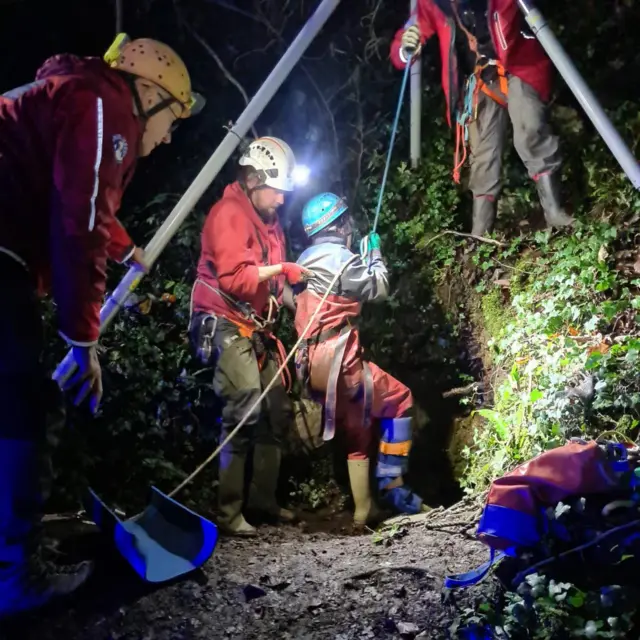 Rescatistas en la oscuridad con faros utilizando un trípode con un cabrestante instalado sobre la entrada del pozo