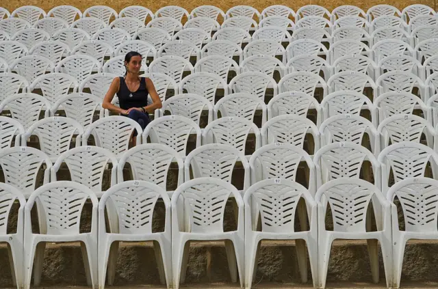 Una mujere sentada rodeada de sillas Monobloc.