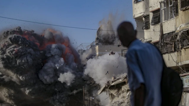 Patlayan bir binayı tam o anda izleyen bir erkeği arkada flu şekilde görüyoruz.