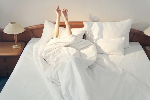 Kobieta w łóżku pod kołdrą w pokoju hotelowym, budząca się rano.