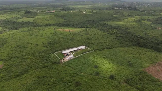 Vue aérienne montrant une vaste forêt verdoyante avec un ensemble de bâtiments au centre, entouré d'un mur.