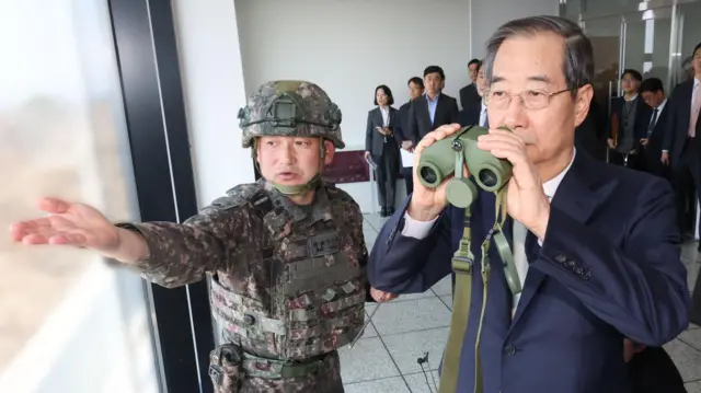 هان داک-سو رئیس‌جمهور موقت کره جنوبی (راست) که مقام نخست‌وزیری را نیز دارد، در جریان دیداری از ایستگاه مراقبتی دورا در شهر پاجو در مرز کره شمالی در ‍۱ آوریل ۲۰۲۵، دوربینی دوچشمی به دست دارد