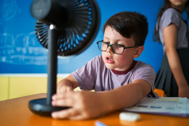 Criança com pequeno ventilador portátil dentro de sala de aula