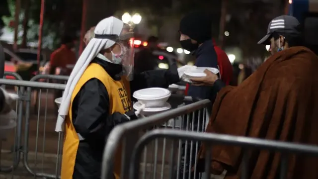 À noite, freira com face shield e máscara contra coronavírus entrega marmitas para 2 homens