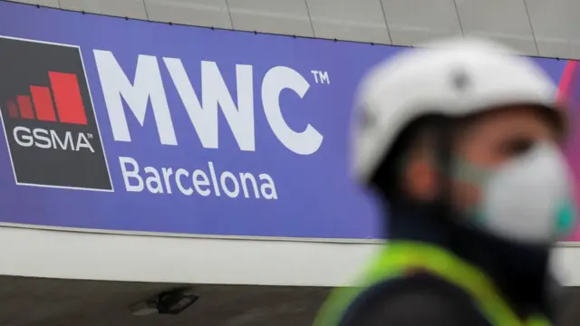 man in mask by a sign for the MWC event in Barcelona, which has been called off