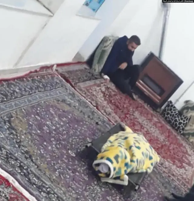 تصویری از شهریار محمدی که در کنار پیکر دوستش محمد حسن‌زاده نشسته است