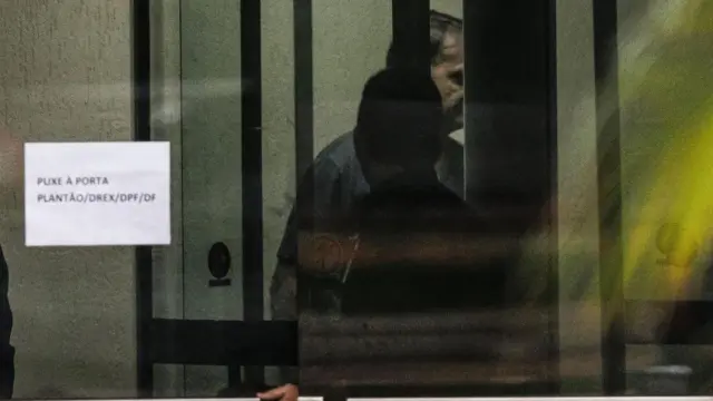 Jair Bolsonaro por trás da porta de vidro da Superintendência da Polícia Federal de Brasília neste domingo.