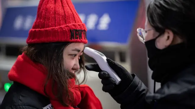 A security personnel (R) checks the temperature of a woman (L) as she travels for the Lunar New Year, at the entrance of Beijing West Railway Station in Beijing