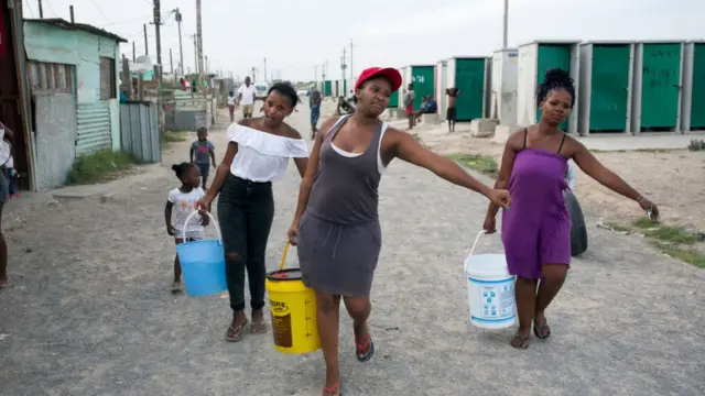 Des femmes vont chercher de l'eau à un robinet communal le 8 février 2018 à Khayelitsha, à environ 40 kilomètres du Cap, en Afrique du Sud.