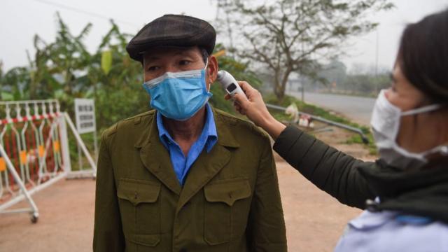 A woman monitors the temperature of a man wearing a mask