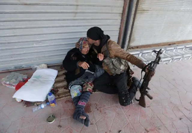 بوسه سرباز ارتش آزاد سوریه بر سر یک زن مسن که در کوچه‌ای در عفرین نشسته است