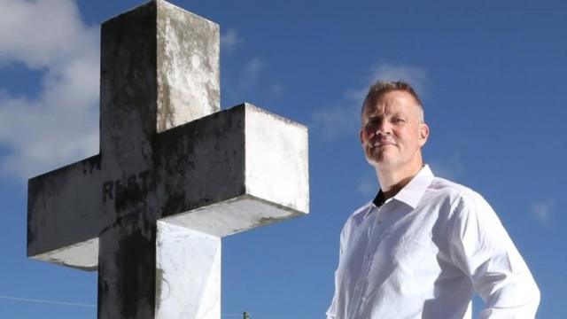 Bill Edgar posa em frente a uma cruz de pedra