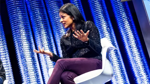 Aparna Bawa dá palestra com os braços abertos e sentada em palco