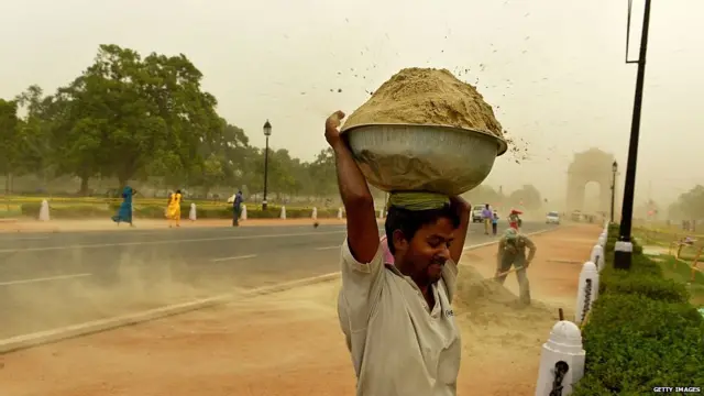 ਝੱਖੜ ਵਿੱਚ ਰੇਤੇ ਦਾ ਬੱਠਲ ਚੁੱਕੀ ਇੱਕ ਮਜਦੂਰ