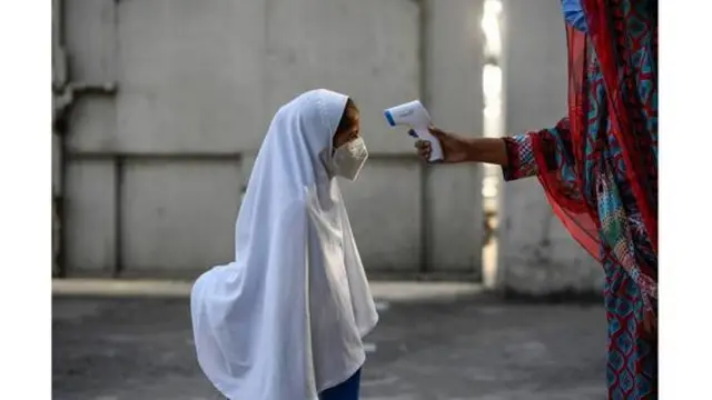 Menina com véu e máscara tem a temperatura medida