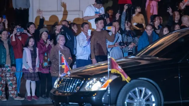 Hanoi residents and members of the media look on as a car believed to be carrying North Korean leader Kim Jong-un passes by after the first meeting between Mr Kim and President Donald Trump at the Hanoi summit on February 27, 2019