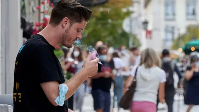 Seorang pria tengah menghisap rokok dengan masker di lengannya