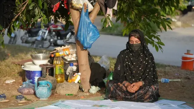 Nazdana sedi pokrivena tufnastim hidžabom i sa maskom na licu, na zemlji sa papirima o razvodu i obrazovanju ispred sebe