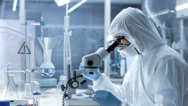 Científico con traje protector mirando una muestra a través de un microscopio