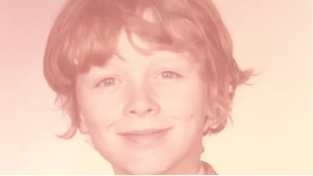 Um menino branco e sorridente olha para a câmera