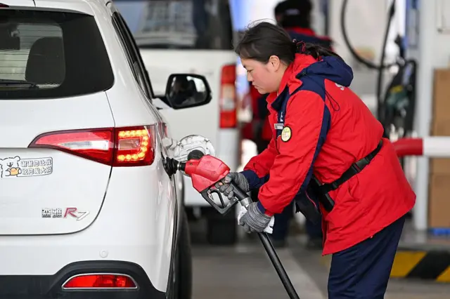 जियांग्सू प्रांत के नांजिंग में 9 मार्च 2026 को एक पेट्रोल पंप पर कार रिफ़िल करती महिला कर्मचारी