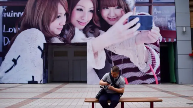 A man looks at his mobile phone in front of a huge poster along a business street in Beijing on May 15, 2018