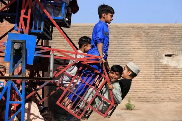 Children enjoy riding a swing during Eid al-Fitr celebrations in Peshawar, Pakistan