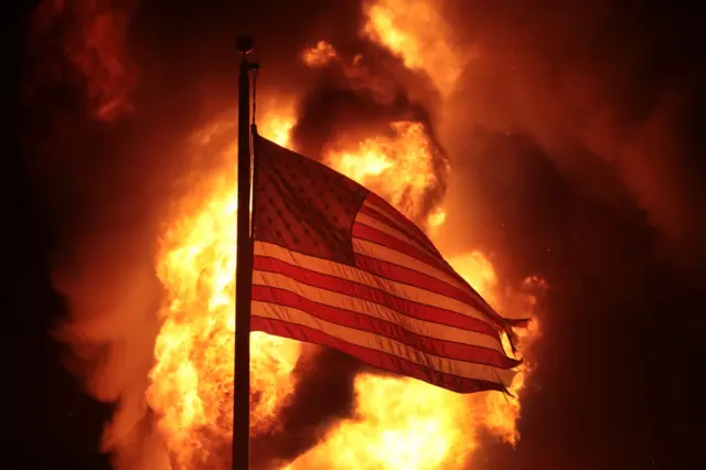 A US flag, with flames in the background