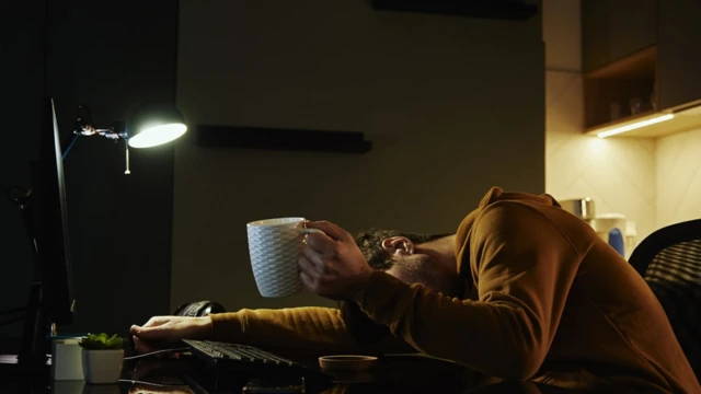 Homme dormant sur son lieu de travail, avec une tasse de café à la main. Freelancer travaillant à distance tard.