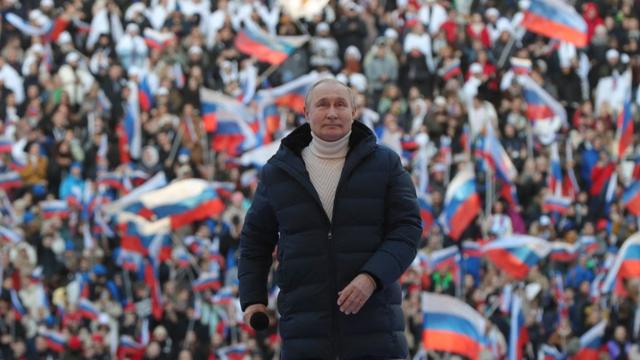 Vladimir Putin con manifestantes en el fondo sosteniendo banderas rusas.