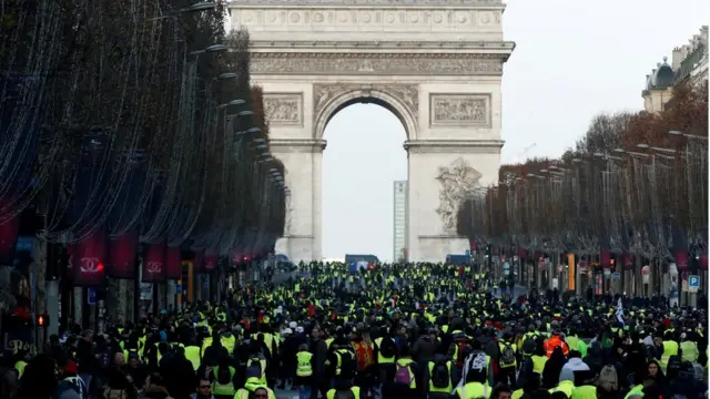 Protesters wearing yellow vests walk on the Champs-Elysees Avenue with the Arc de Triomphe in the background