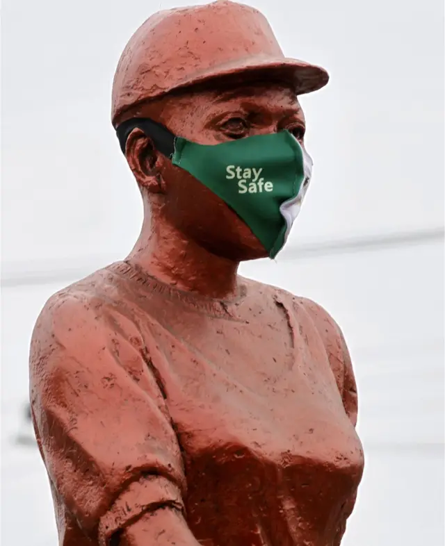Une statue de couleur bronze est munie d'un masque avec une légende qui dit "soyez en sécurité".
