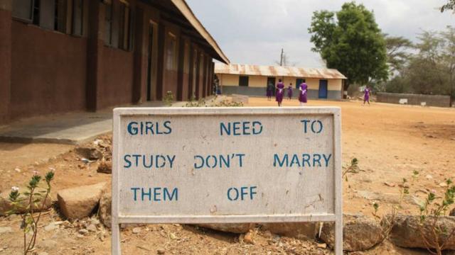 Une cour d'école en Afrique - un panneau d'affichage indique "Les filles ont besoin d'étudier, ne les mariez pas"