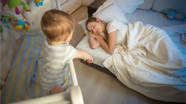 ህጻኑ በራሱ አልጋ ላይ ሆኖ በቅርቡ አልጋዋ ላይ የተኛችውን እናቱን ሲመለከት