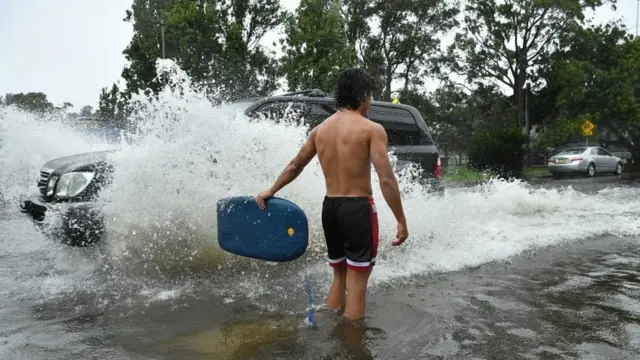 A car passes a man standing in flood water in Sydney, Australia (9 Feb 2020)