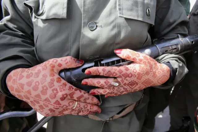 A Sahrawi woman soldier holds a gun. She has henna-dyed patterns on her hands.