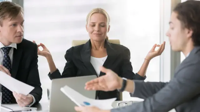 Una mujer hace relajación frente a dos hombres que discuten.