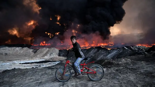 தாக்குதலின்போது தீ பரவிய எண்ணெய் வயலை கடந்து செல்லும் சிறுவன்