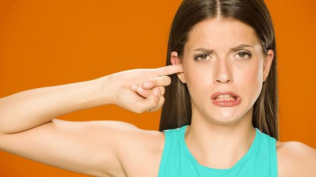 Em foto de estúdio, mulher coloca dedo no ouvido