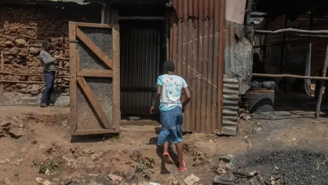 A woman carrying a Jerrycan of water walks into a local public toilet in Kibera