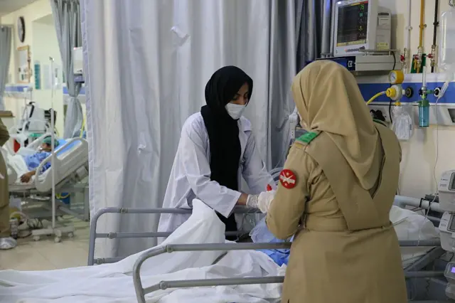 یوه ښځه پوځۍ جامه کې به هم روغتیايي جامو کې د ټپي کټ ته ولاړې دي.