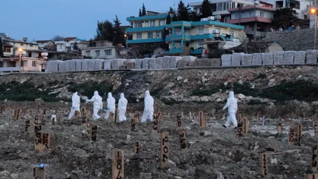 Des travailleurs en costume blanc marchent dans le cimetière de Narlica